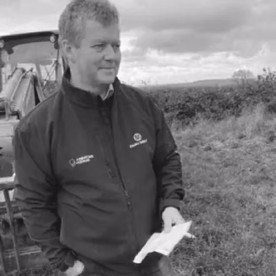 Bryan Harris stands beside farm machinery, holding a sheet of paper.