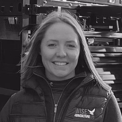 Laura Wise smiles in a padded jacket with the Wise Agriculture Co logo.