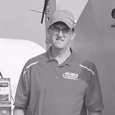Marlin Huber stands beside livestock feeding equipment, wearing a Huber Equipment shirt.
