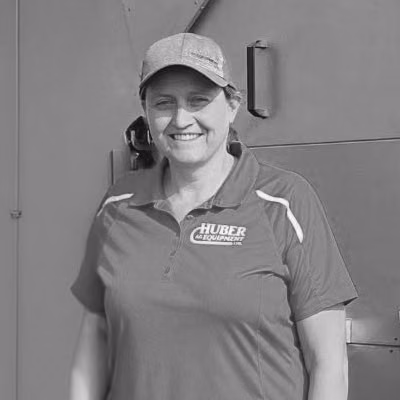Myrna Huber beside a metal livestock feeder, wearing a Huber polo shirt.