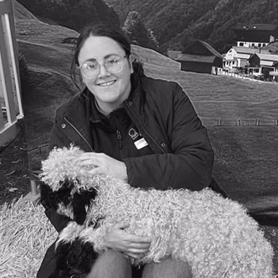 A woman holds a sheep in a rural paddock.